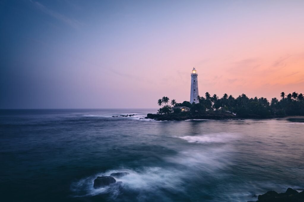 Illuminated lighthouse in the middle of palm trees. South coast of Sri Lanka at sunset.
